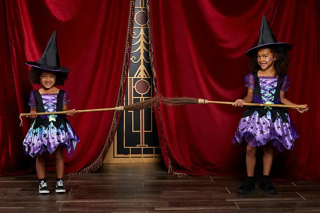 Two cute witches holding broomsticks between them